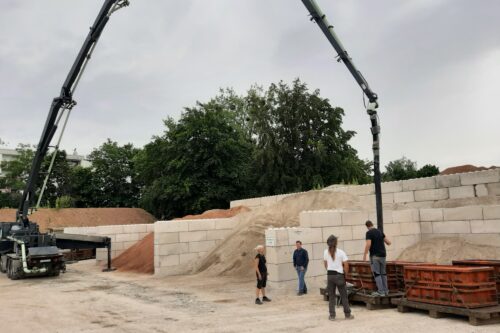 4 persons standing around a concrete pump filling a steel mould